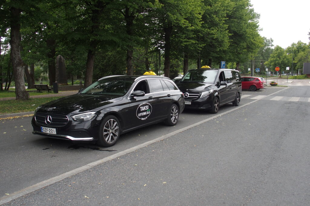 Kaksi mustaa Mercedes Benz -autoa taksitolpalla.