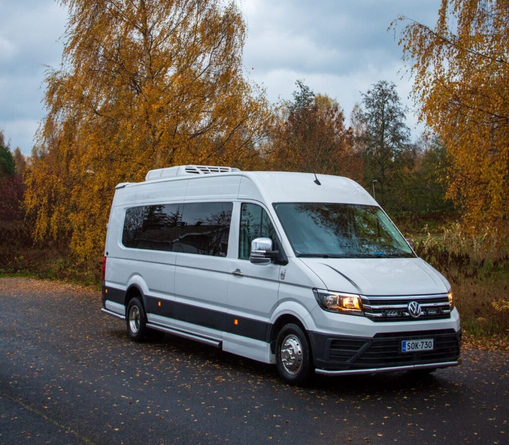 Valkoinen Volkswagen Crafter pikkubussi syksyisessä maisemassa.